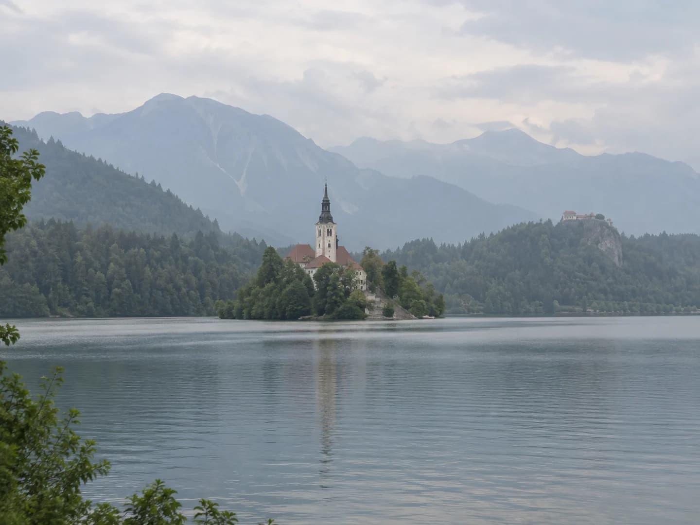 Low-contrast alpine lake photo with a church island and hazy mountains