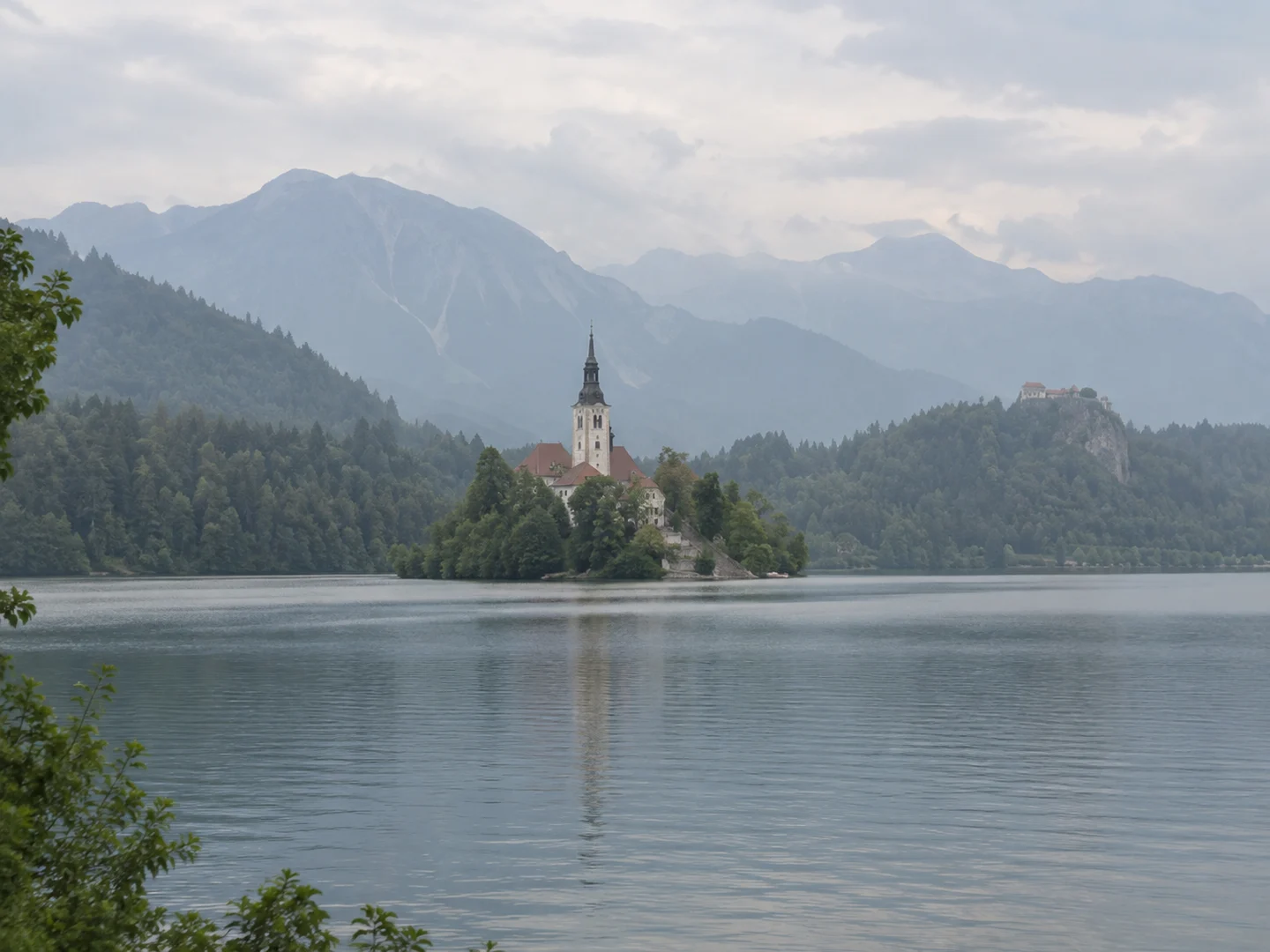 Low-contrast alpine lake photo with a church island and hazy mountains